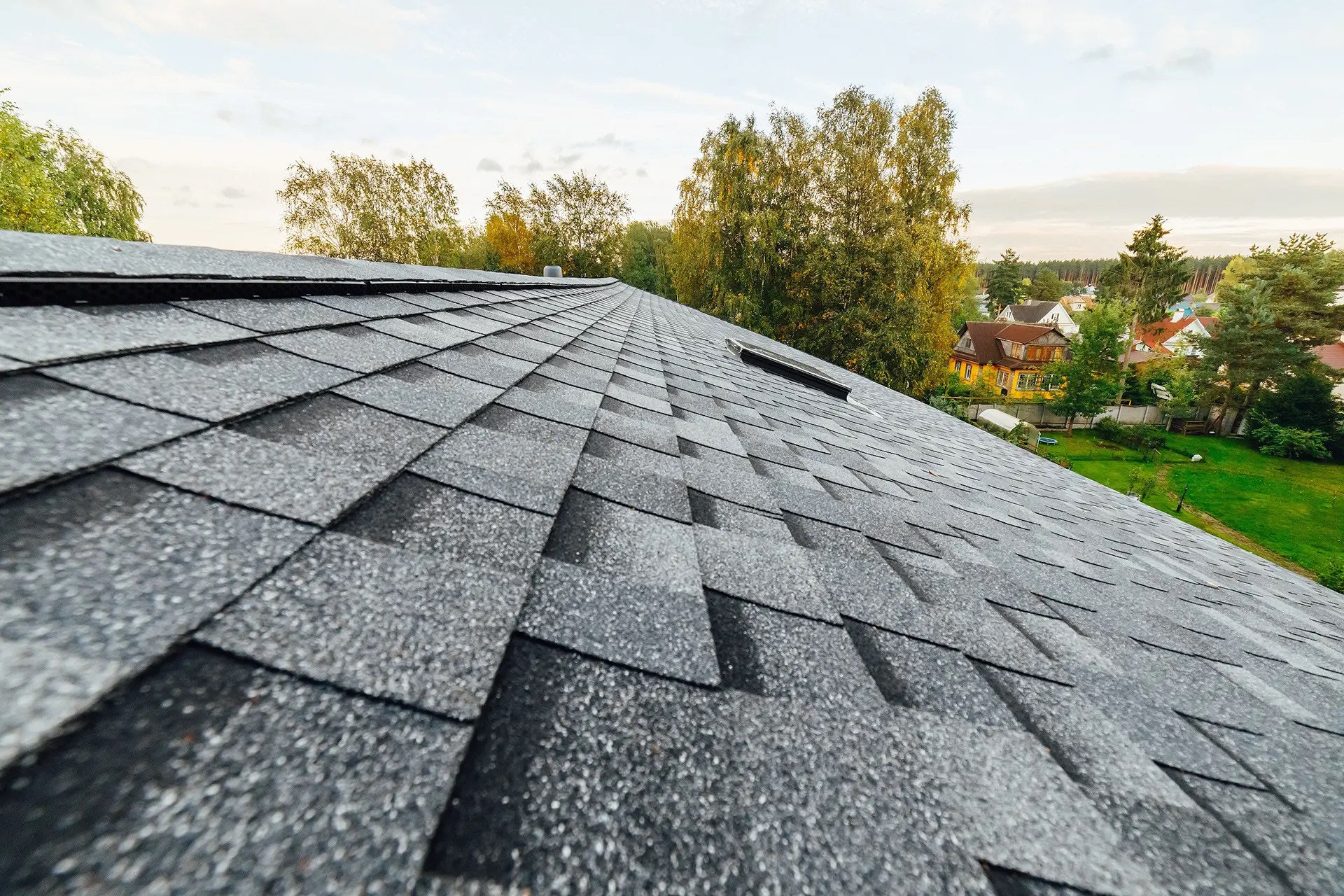 Freshly finished asphalt shingle roof ridge at golden hour, overlooking Sacramento-area homes and trees